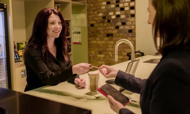 Woman paying for a TopBrewer coffee next to a TopBrewer machine
