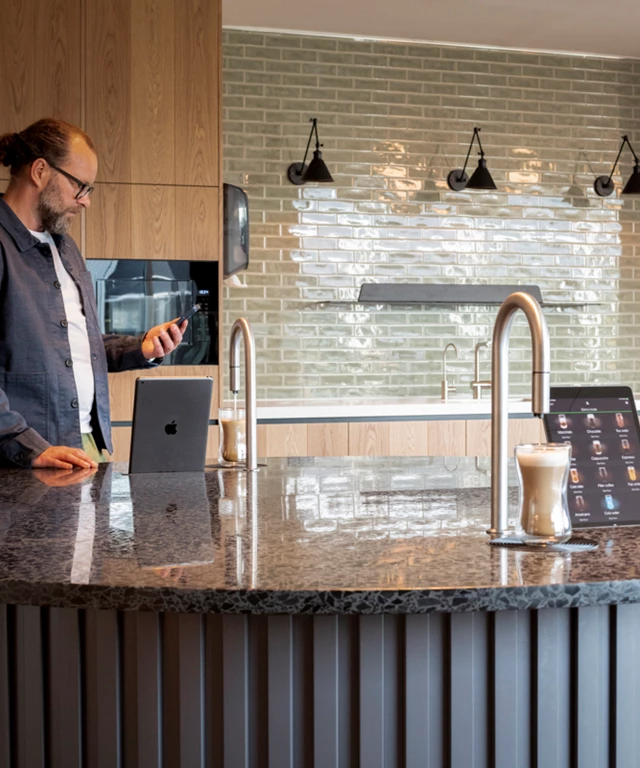 2 TopBrewer coffee machines built into a circular island, with a man in the background looking at his phone