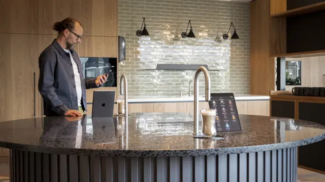 2 TopBrewer coffee machines built into a circular island, with a man in the background looking at his phone